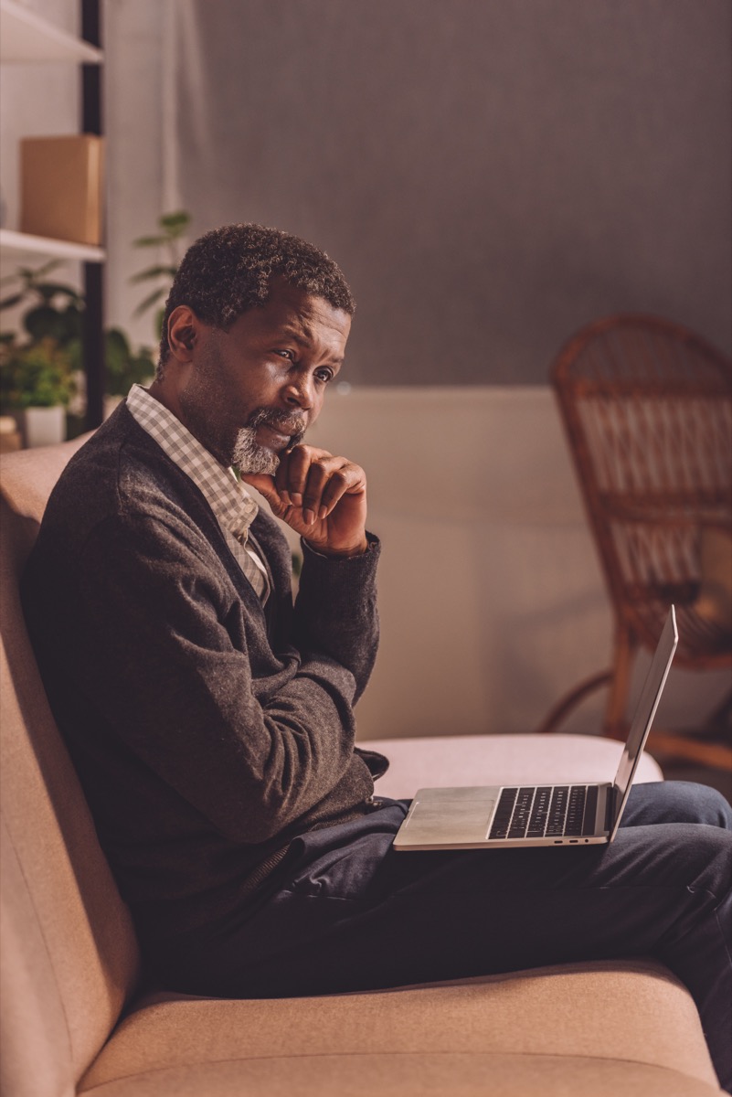 upset african american man sitting on sofa with laptop at night
